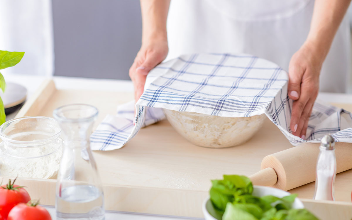 Baketips for gjærbakst -foto av kjøkkenhåndklede over en bakebolle med deig.