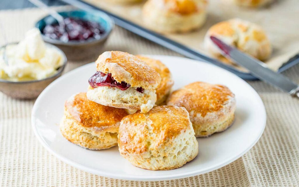 Nystekte grove scones med syltetøy på en hvit asjett.