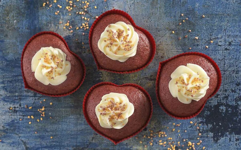 Nystekte red velvet muffins med krem og kakepynt i røde hjerteformer.