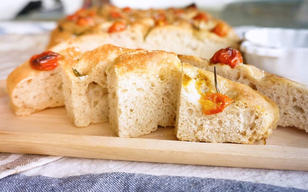 Oppskåret saftig focaccia med cherrytomater på en trefjøl.